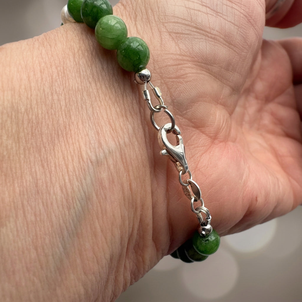 Close-up of the silver-coloured lobster clasp and connecting links on a green jade bracelet worn on a wrist.