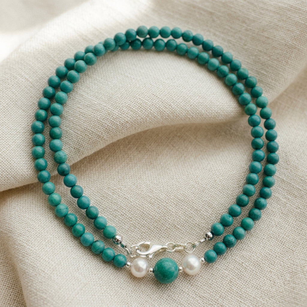 Hubei turquoise necklace arranged in overlapping loops on cream linen, showing two white baroque pearls, a larger turquoise bead and a sterling silver clasp.