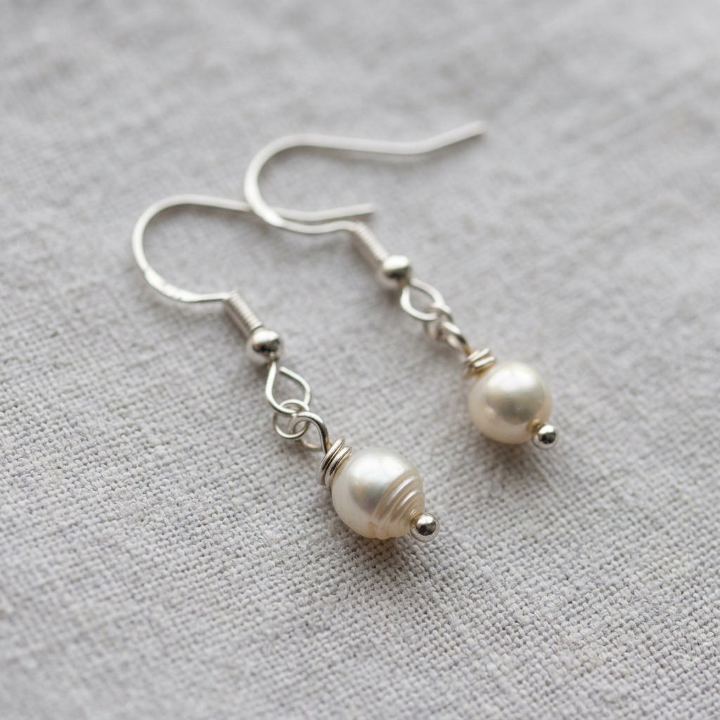 Pair of white baroque pearl drop earrings on pale linen, showing irregular lustrous pearls, sterling silver hooks, connecting links and small silver bead tips.