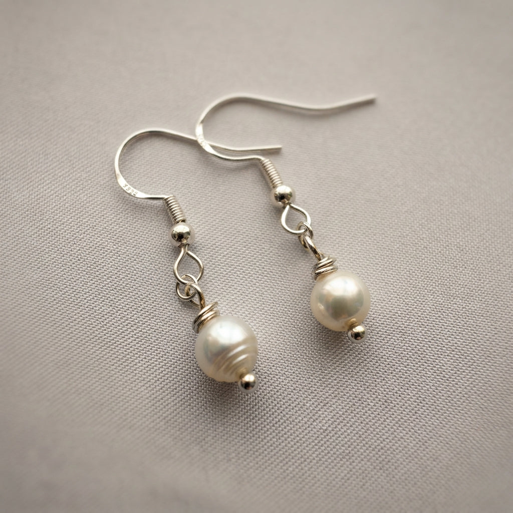 Pair of white baroque pearl drop earrings on pale fabric, showing naturally uneven pearls with soft lustre, sterling silver hooks and wire-wrapped connecting links.