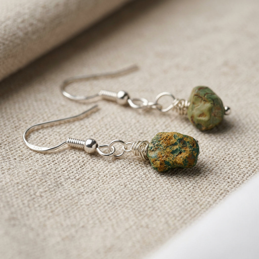 Raw Hubei turquoise drop earrings with green-blue stones, earthy brown matrix and sterling silver hooks, resting on cream linen.