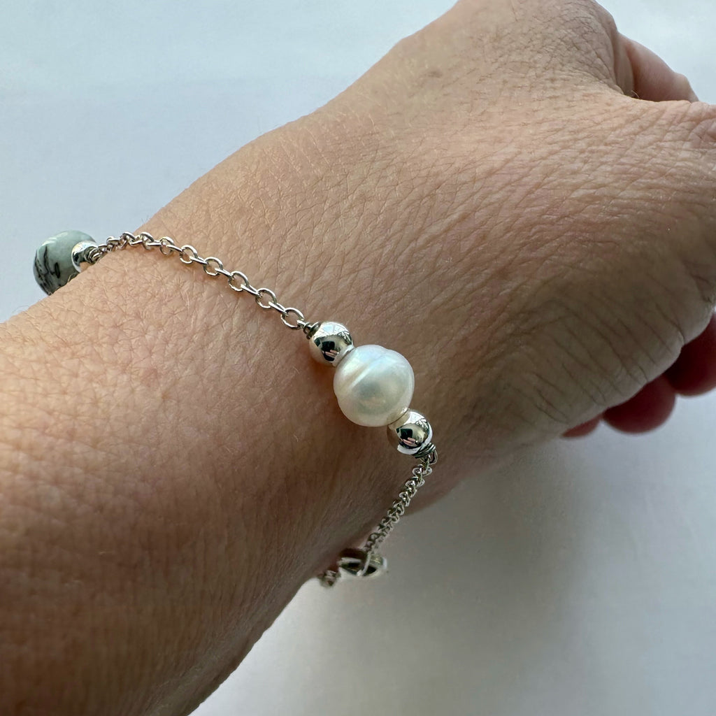 Close-up of a white baroque pearl between polished sterling silver spacers on a chain bracelet worn on a wrist.