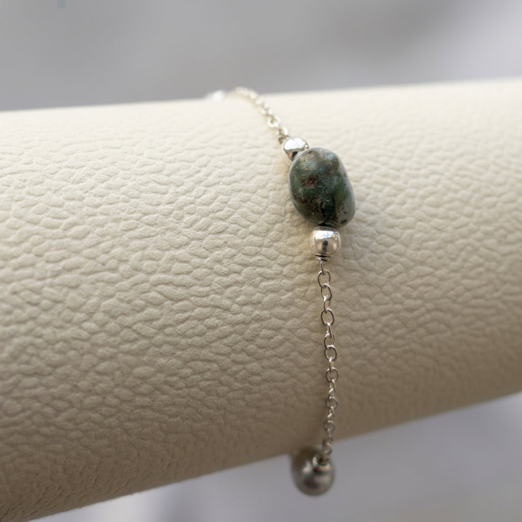 Close-up of an oval larimar bead with dark grey-green markings between sterling silver spacers on a cream bracelet display.
