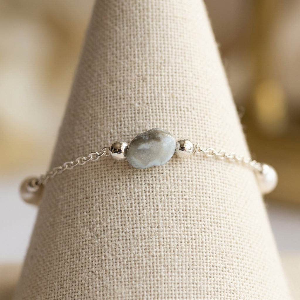 Sterling silver chain bracelet with a pale blue larimar bead and white baroque pearl accents on a cream linen display.