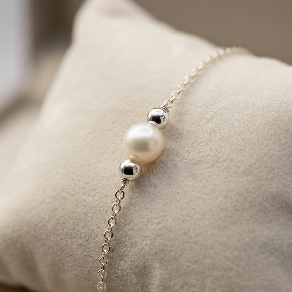 White baroque pearl between polished sterling silver spacers on a delicate chain bracelet, resting on a cream cushion.