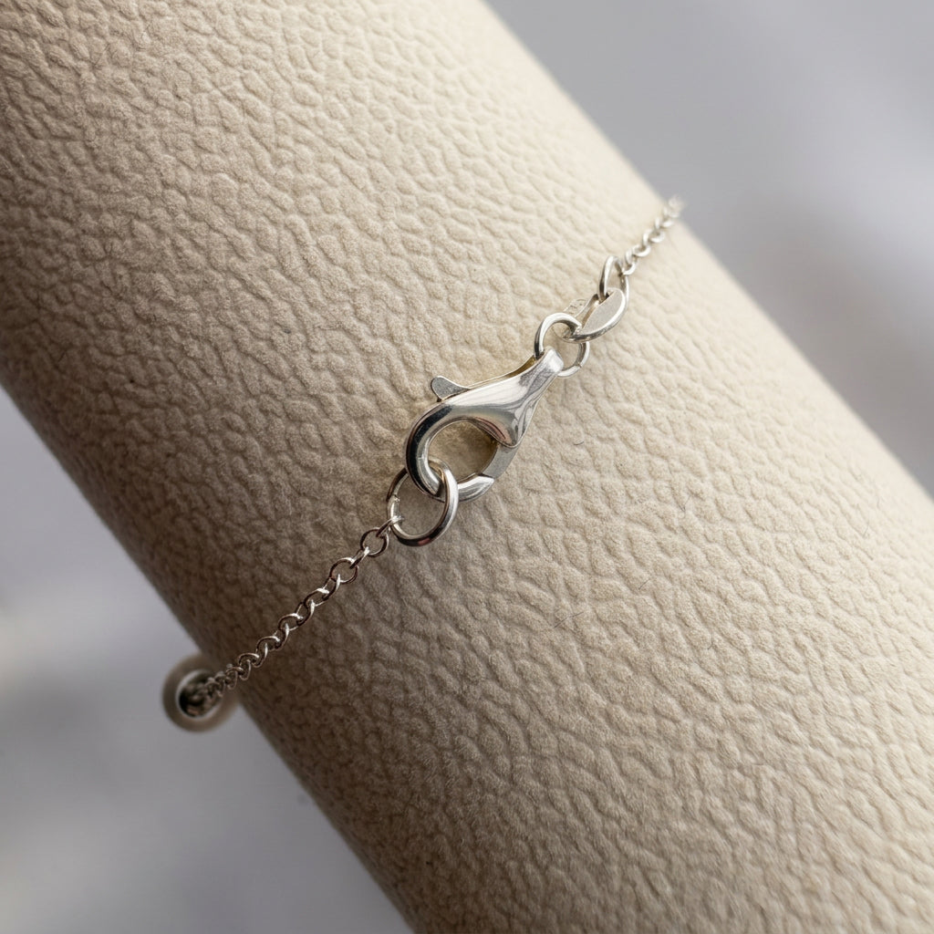 Close-up of the sterling silver lobster clasp and connecting rings on a delicate chain bracelet, resting on a cream display.