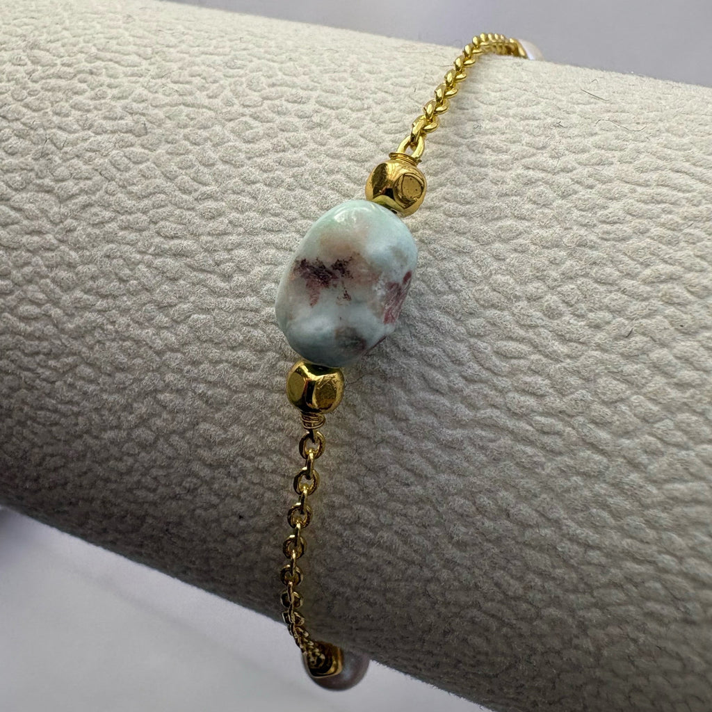 Close-up of a pale blue larimar bead with dark markings between gold-coloured spacers on a gold-filled bracelet display.
