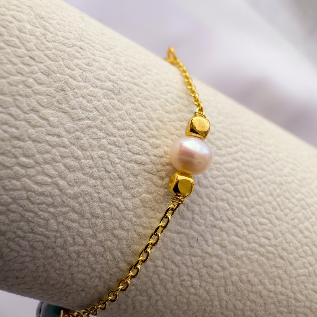 Close-up of an oval pale blue larimar bead with dark markings between gold-coloured spacers on a cream bracelet display.