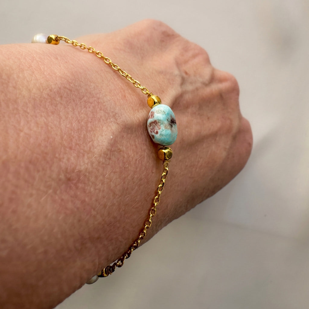 Gold-filled chain bracelet worn on a wrist, featuring an oval blue larimar bead with white and brown markings between gold-coloured spacers.