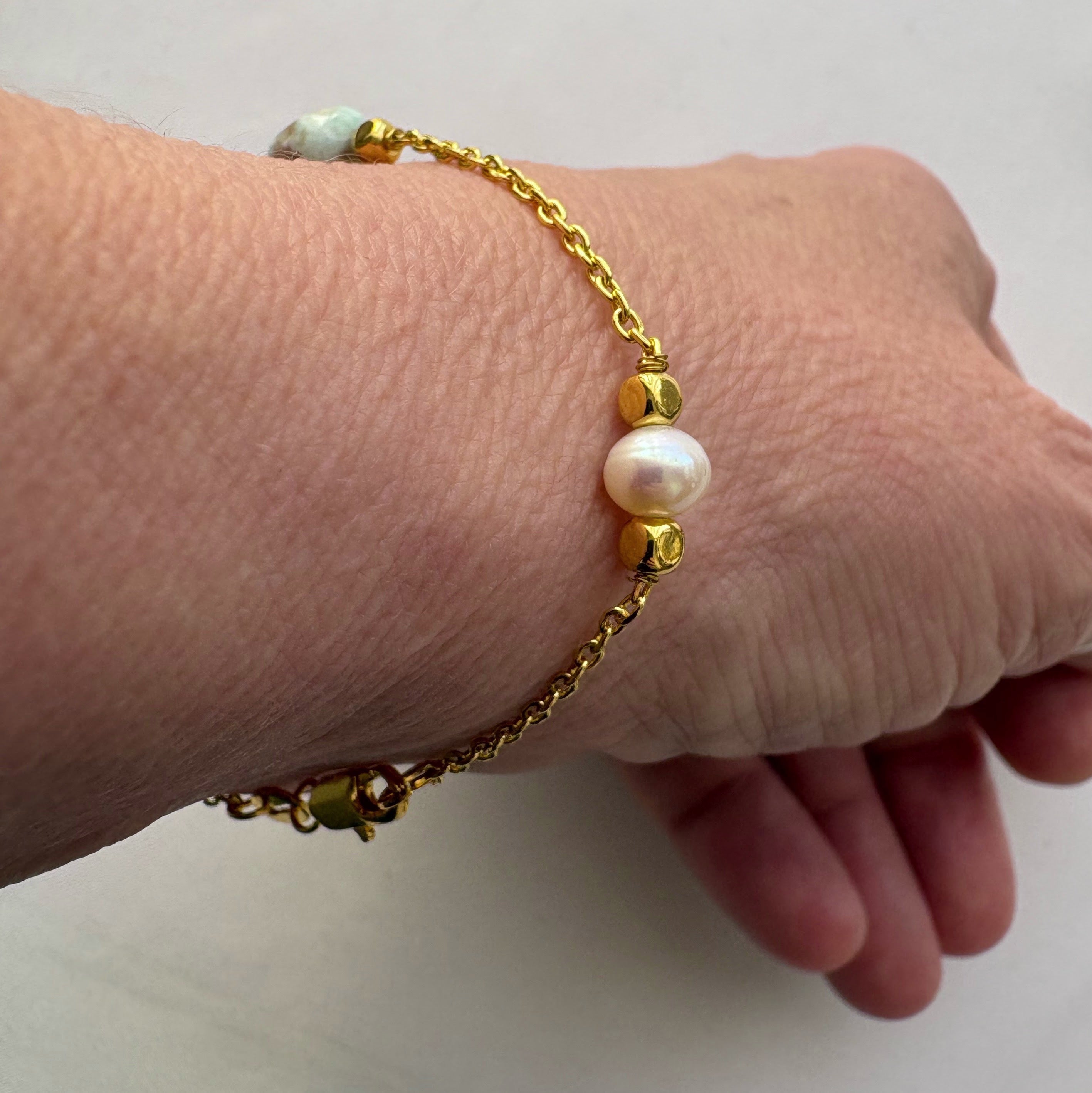 Gold-filled chain bracelet worn on a wrist, showing a white baroque pearl between faceted gold-filled spacer beads.