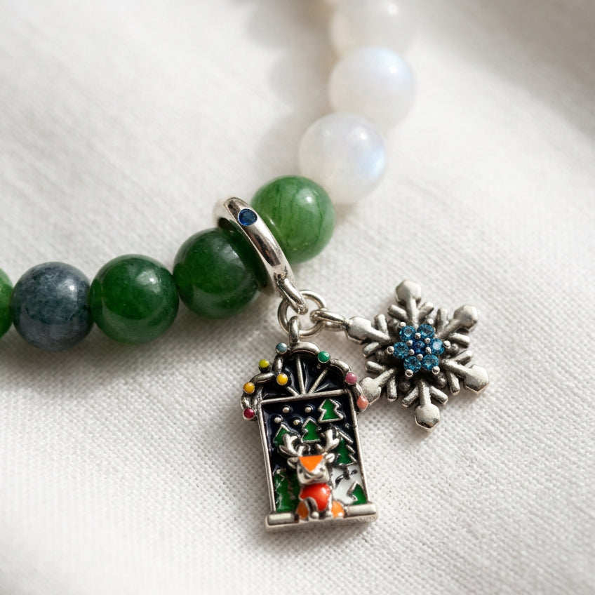 Close-up of a blue crystal snowflake and colourful reindeer Advent window charms on a white and green jade bracelet.