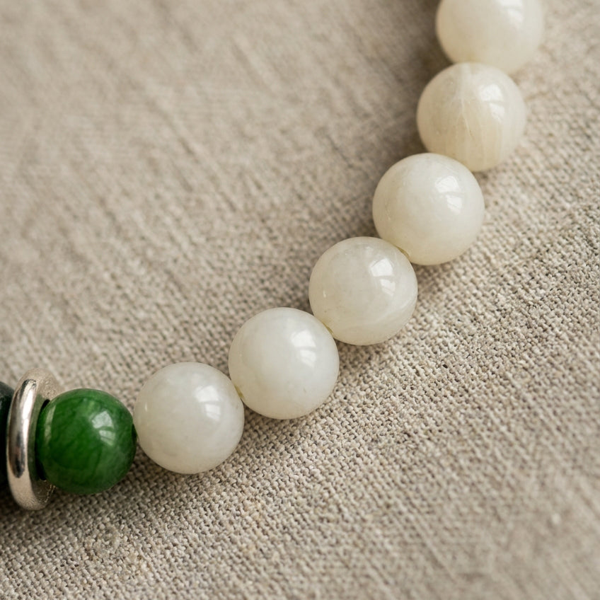 Close-up of polished white jade beads beside a green jade bead on beige linen.