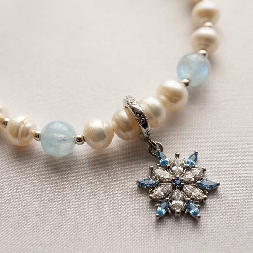 Close-up of a blue and clear crystal snowflake charm on an aquamarine and white baroque pearl bracelet with sterling silver fittings.