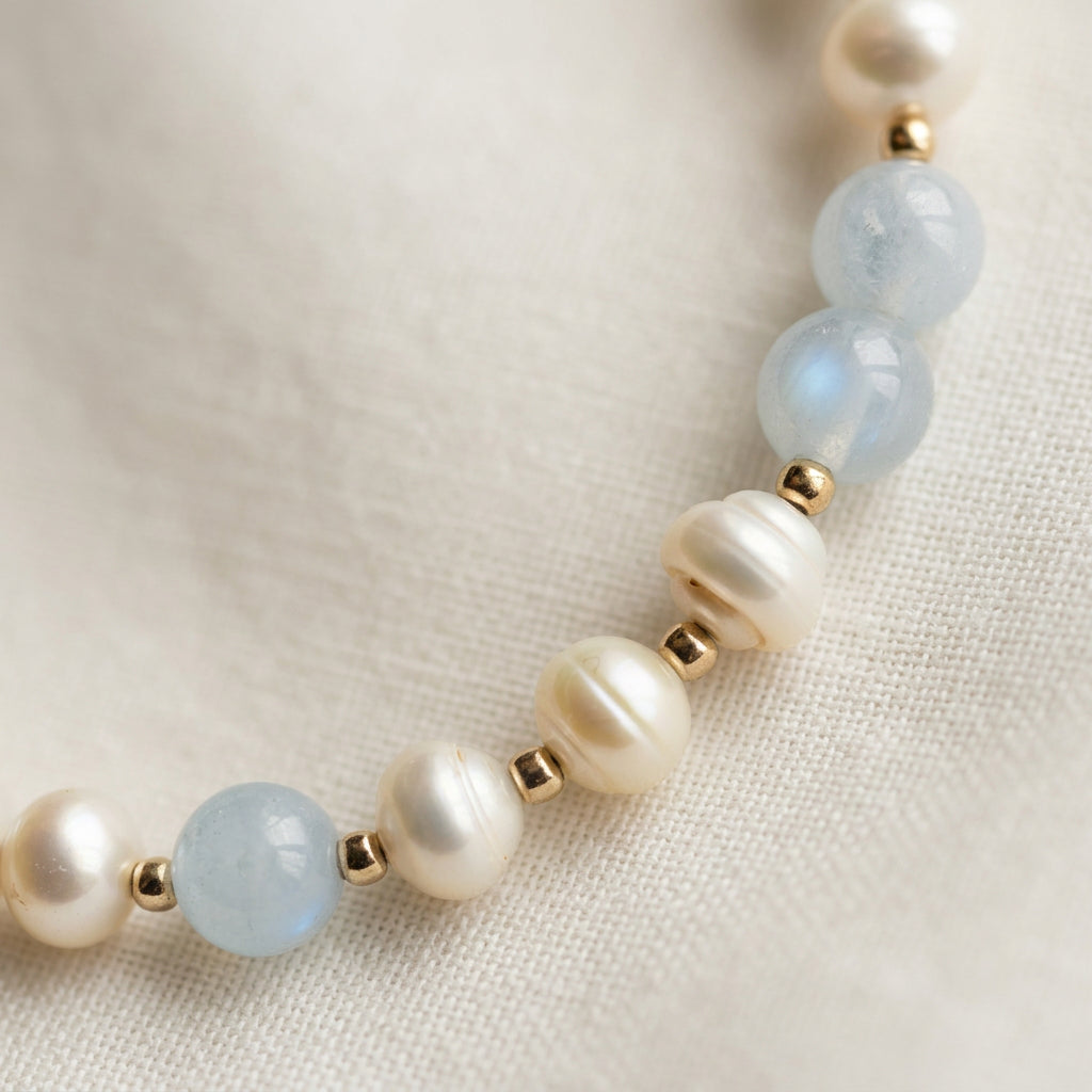 Close-up of pale blue aquamarine beads and white baroque pearls with sterling silver spacers on cream fabric.