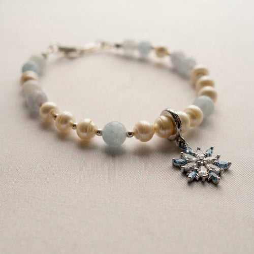 Aquamarine and white baroque pearl bracelet with sterling silver fittings and a crystal snowflake charm, resting on pale fabric.