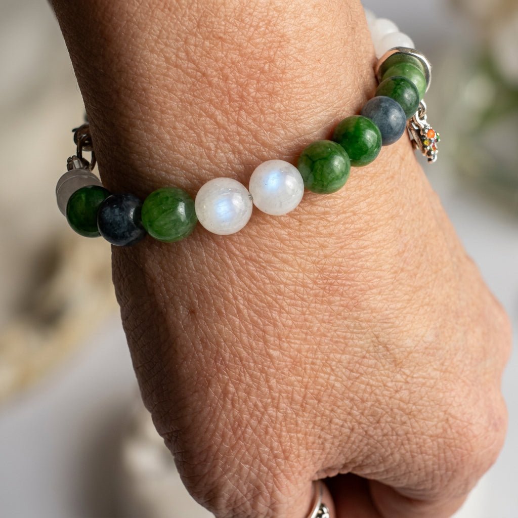 White and green jade bracelet with dark blue tourmaline beads, worn on a wrist with the charms hanging to one side.⠋