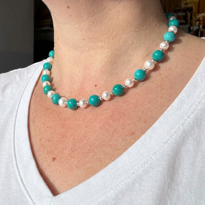 Angled view of the Hubei turquoise and white baroque pearl necklace worn with a white V-neck top.