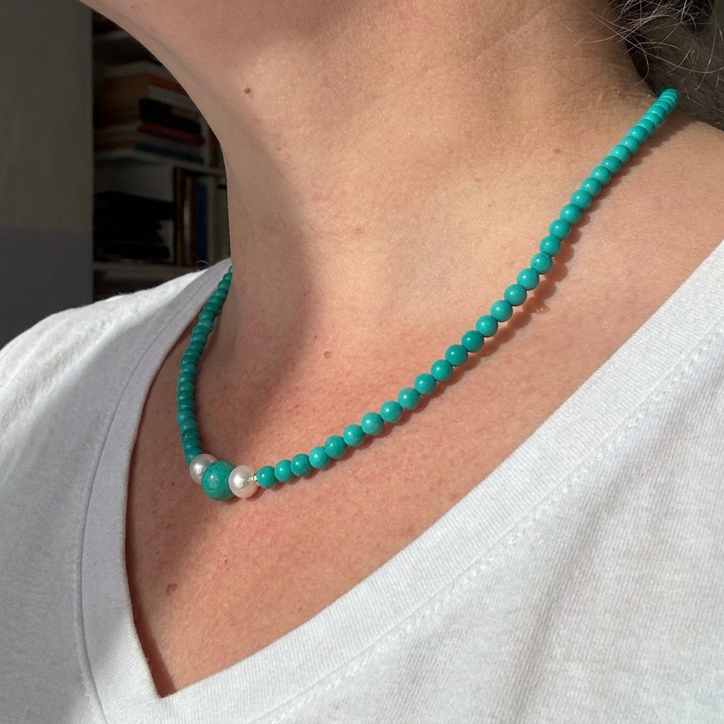 Side view of the Hubei turquoise necklace worn with a white V-neck top, showing small turquoise beads and the central pearl detail.