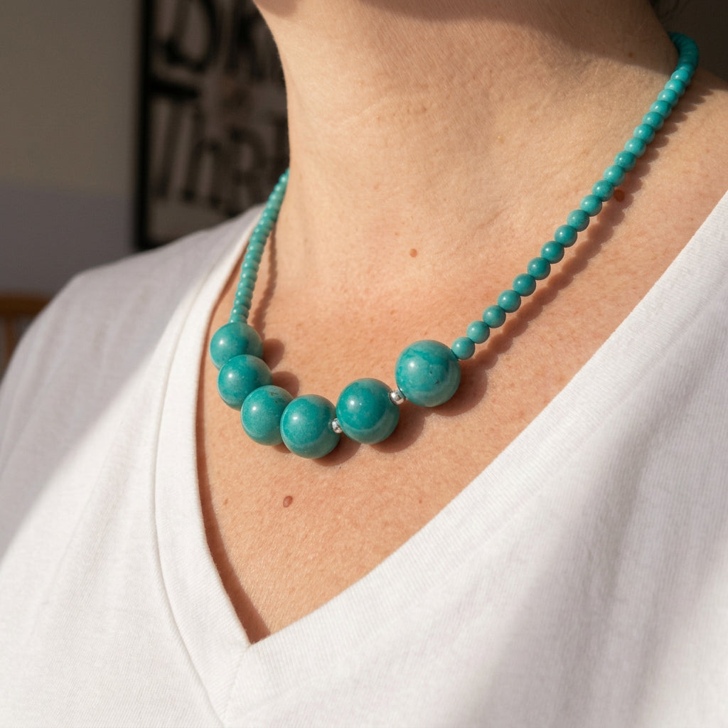 Side view of the turquoise necklace worn with a white V-neck top, showing the contrast between the large central beads and smaller beads.
