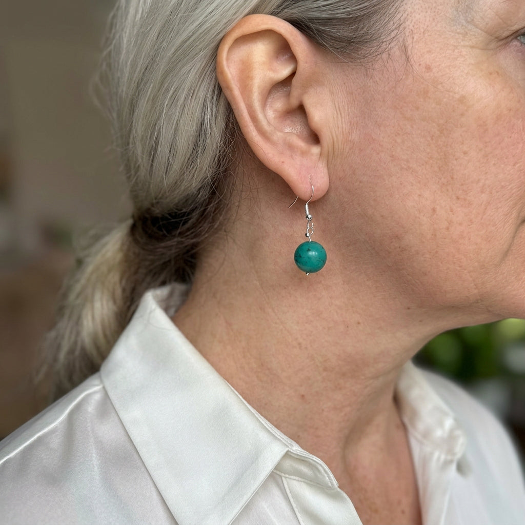 Hubei turquoise drop earring worn on the ear, showing a single green-blue bead suspended from a sterling silver hook.