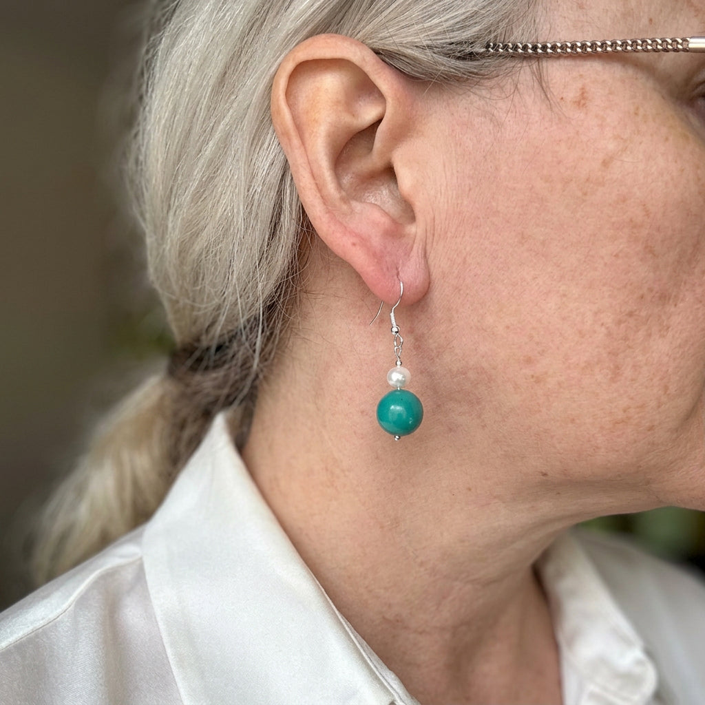 Sterling silver drop earring worn on the ear, with a white baroque pearl above a larger green-blue Hubei turquoise bead.