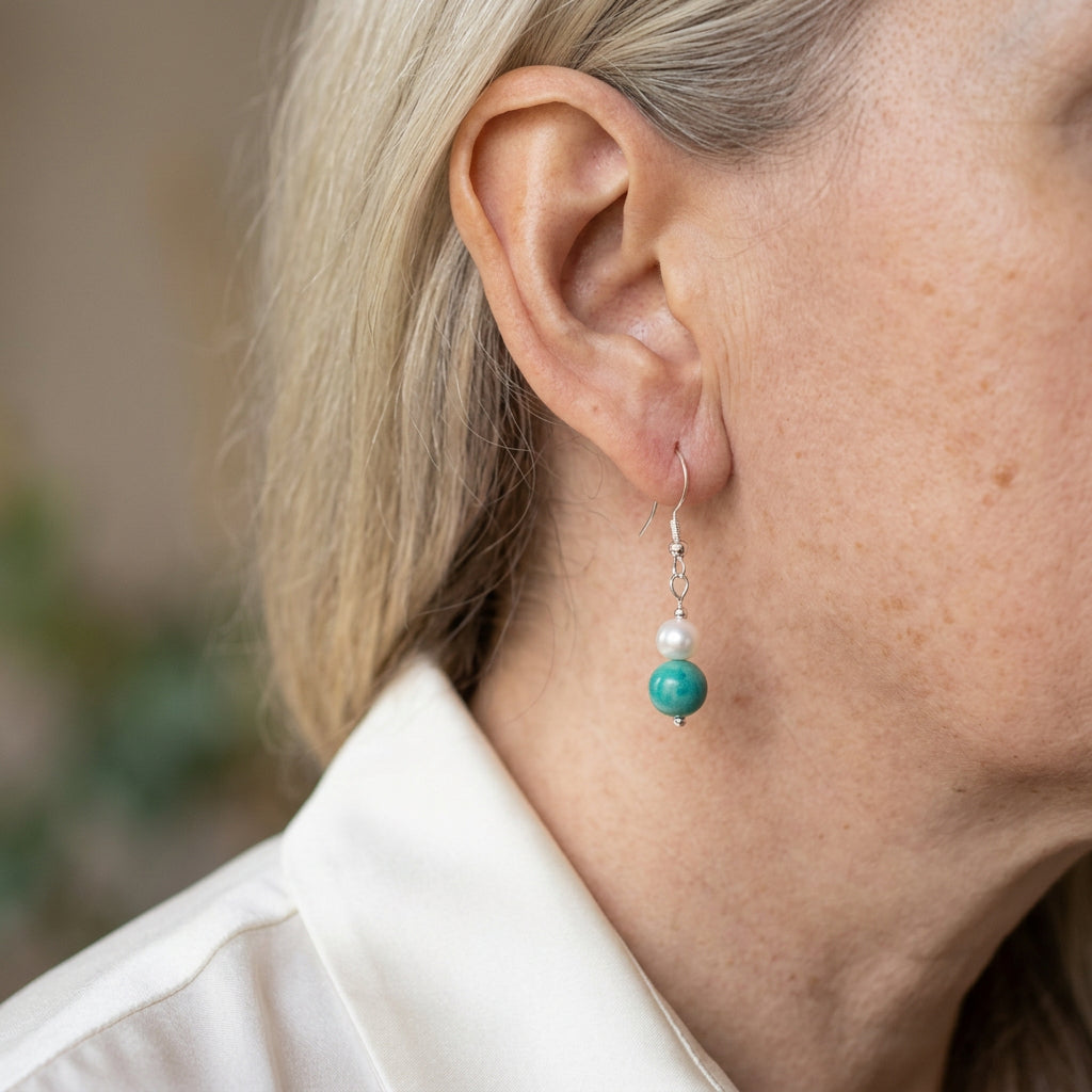 White baroque pearl and turquoise drop earring worn on the ear, with a small white pearl above a larger green-blue turquoise bead and sterling silver hook.