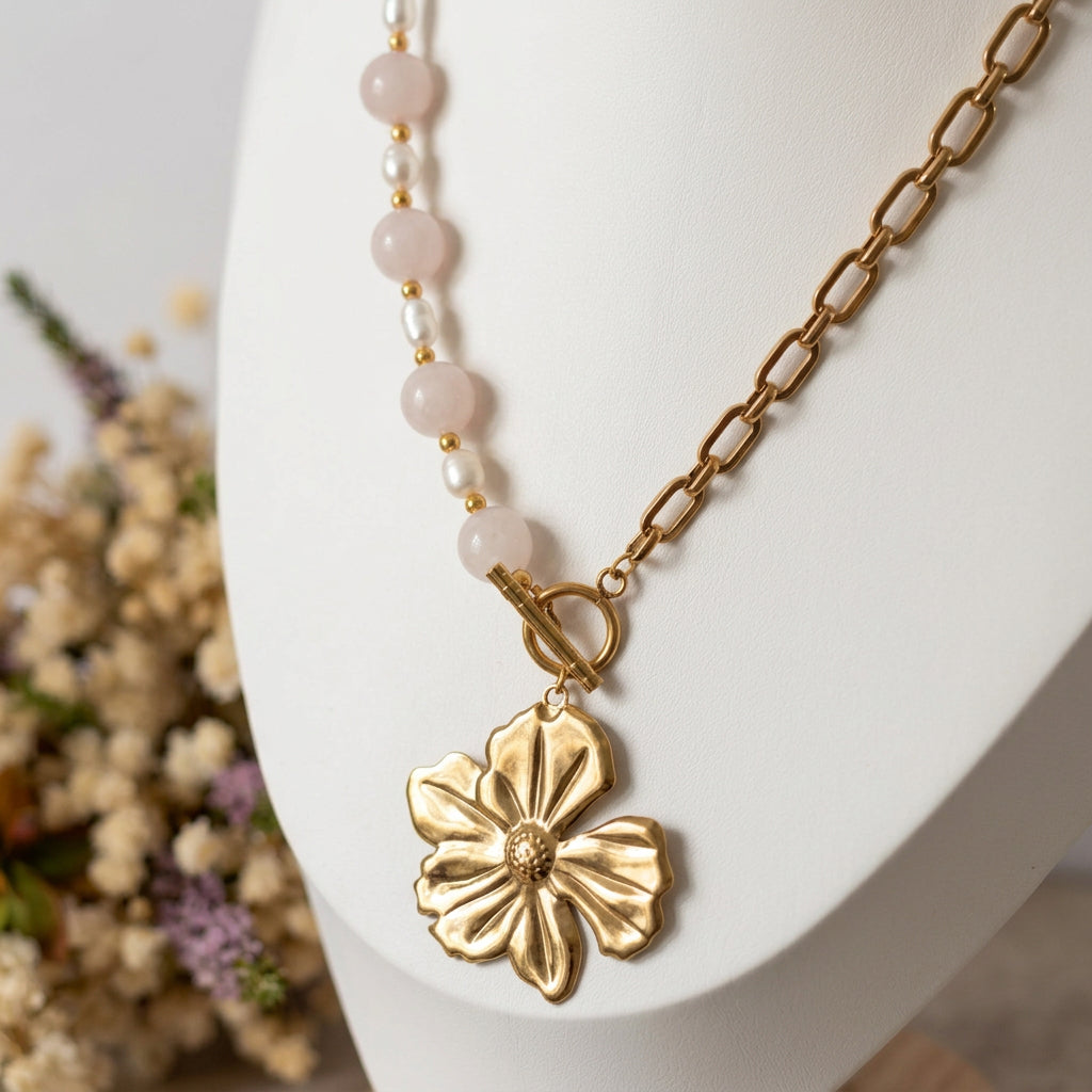 Pink quartz and white baroque pearl necklace with a gold-plated paperclip chain, fastened front toggle and five-petal flower pendant, displayed on a white jewellery bust beside dried flowers.
