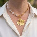 Pink quartz and white baroque pearl necklace with a gold-plated paperclip chain, fastened at the front with a toggle clasp and large sculpted flower pendant, worn with an open-neck white shirt.