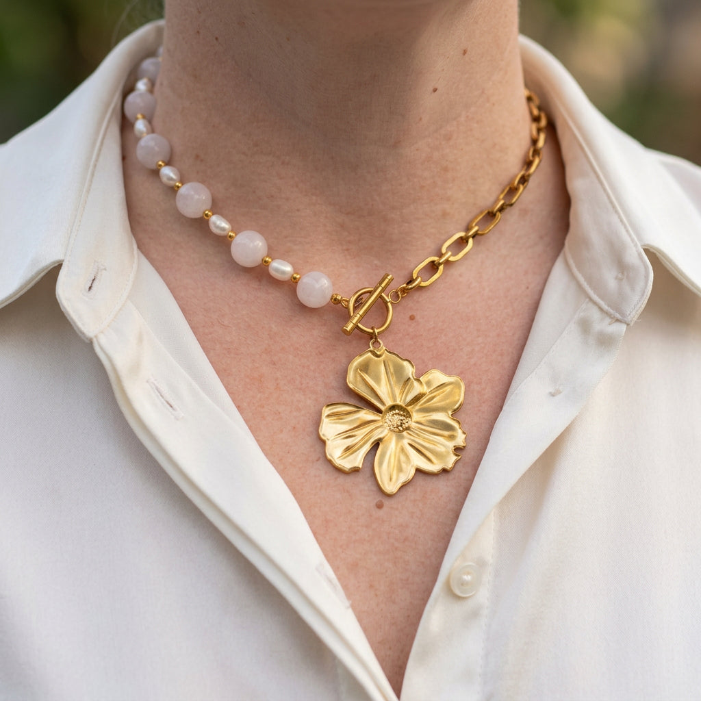 Pink quartz and white baroque pearl necklace with a gold-plated paperclip chain, fastened at the front with a toggle clasp and large sculpted flower pendant, worn with an open-neck white shirt.