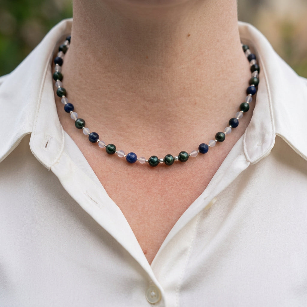 Deep green peacock pearls, blue lapis lazuli and pale moonstone beads with small sterling silver spacers, worn as a necklace with an open-neck white shirt.