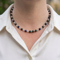 Deep green peacock pearls, blue lapis lazuli and pale moonstone beads with small sterling silver spacers, worn as a necklace with an open-neck white shirt.