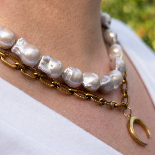Side view of a double-layer necklace worn with a white top, showing large irregular silvery-white keshi pearls above a gold-plated paperclip chain and crescent moon pendant.