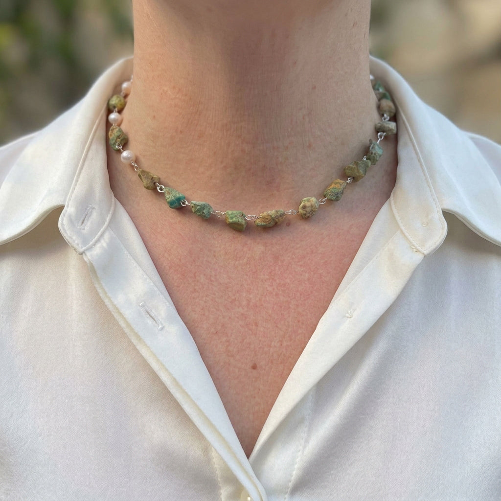 Raw Hubei turquoise and white baroque pearl necklace worn with an open-neck white shirt, showing irregular green-blue stones with brown matrix, three white pearls along one side and handmade sterling silver wire links.