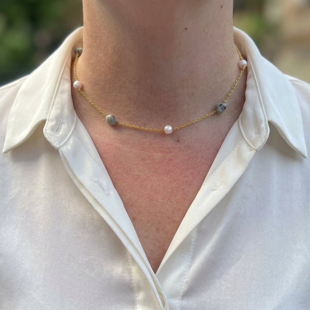 White baroque pearls alternating with irregular blue-grey larimar stones along a delicate gold-filled chain, worn at the collarbone with an open-neck white shirt.