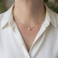 Single white Akoya pearl set at the centre of a delicate gold-filled chain, worn at the collarbone with an open-neck white silk shirt.