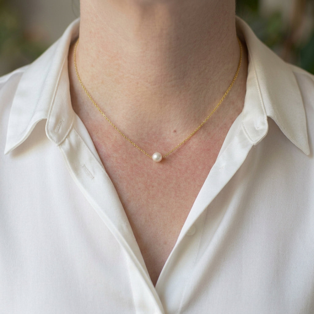 Single white Akoya pearl set at the centre of a delicate gold-filled chain, worn at the collarbone with an open-neck white silk shirt.