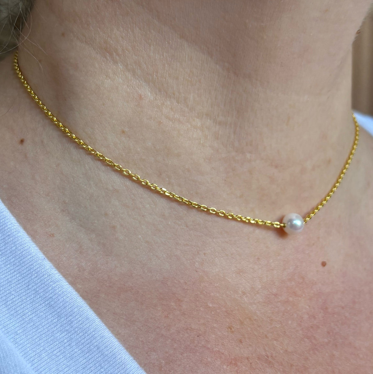 Angled close-up of a single white Akoya pearl necklace worn with a white top, showing the lustrous round pearl set directly on a gold-filled chain.