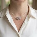 Large lavender keshi pearl set at the centre of a delicate sterling silver chain, worn with an open-neck white shirt, showing its irregular ruffled shape and silvery-purple lustre.