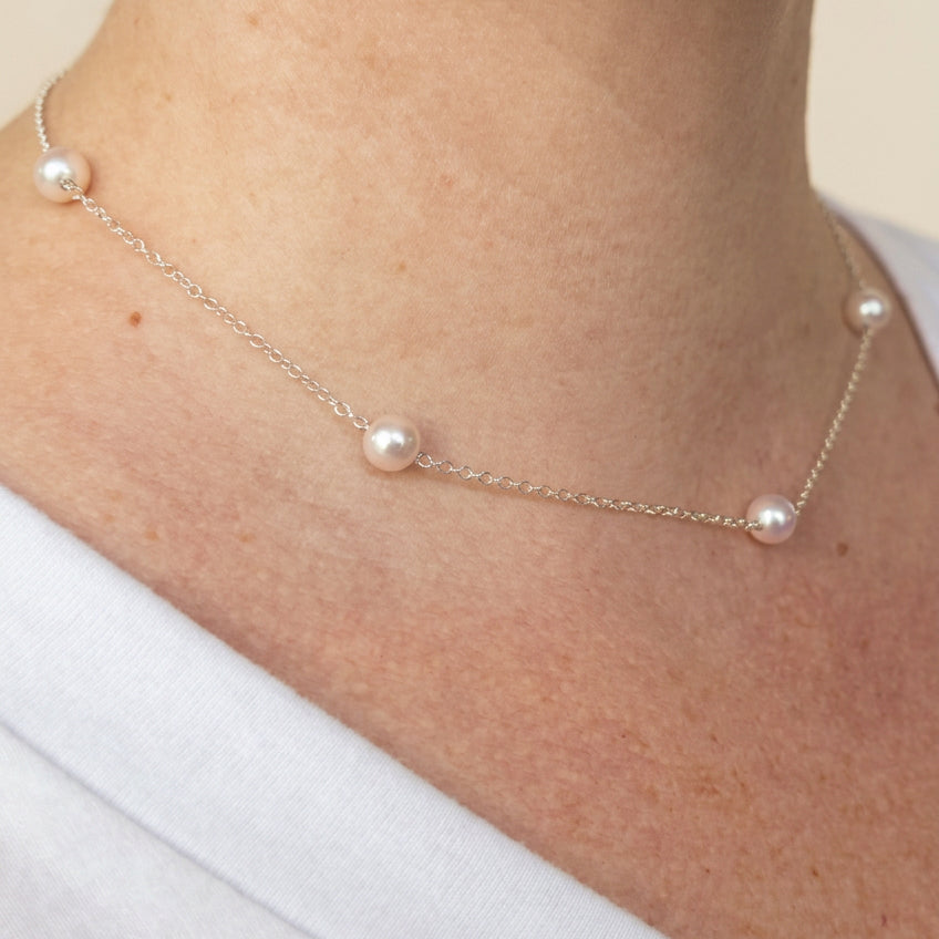Angled close-up of an Akoya pearl station necklace worn with a white top, showing lustrous round white pearls spaced along a fine sterling silver chain.