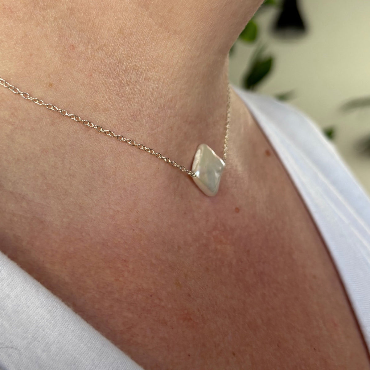 Side-angle close-up of a white square baroque pearl necklace worn with a white top, showing the pearl’s flat profile on a fine sterling silver chain.