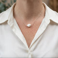 Single white baroque pearl set at the centre of a delicate sterling silver chain, worn with an open-neck white shirt, showing the pearl’s irregular shape and creamy iridescent lustre.⠋