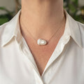 Large white keshi pearl set at the centre of a delicate sterling silver chain, worn with an open-neck white shirt, showing its irregular cloud-like shape and soft iridescent lustre.⠋