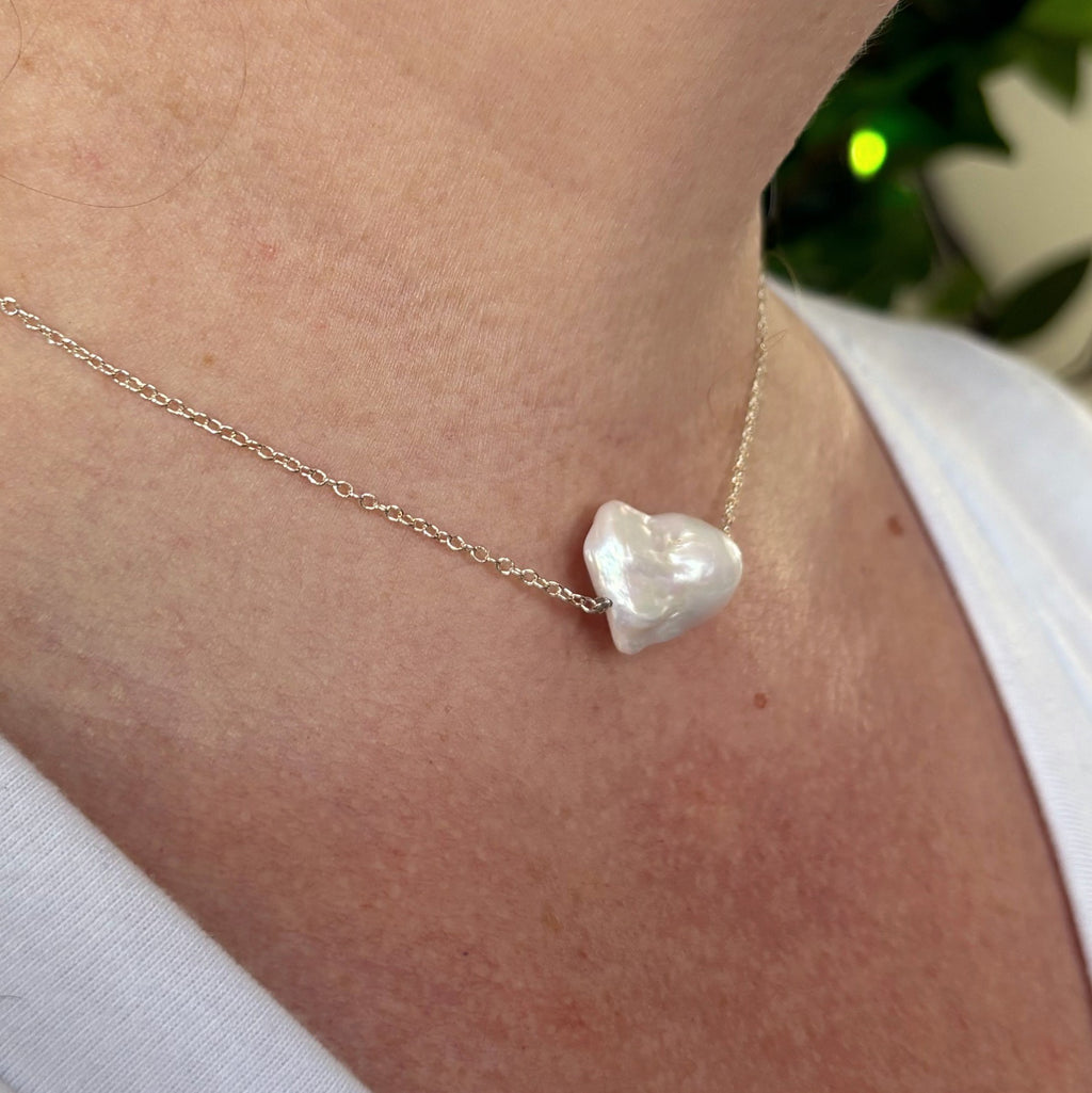 Angled close-up of a white Keshi pearl necklace worn with a white top, showing the pearl’s sculptural profile and lustrous surface on a fine sterling silver chain.⠋