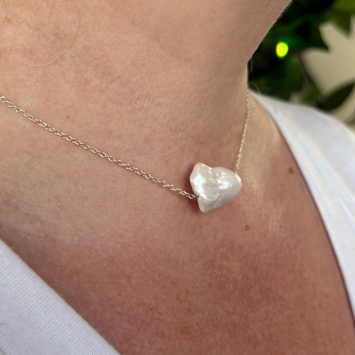 Angled close-up of a white Keshi pearl necklace worn with a white top, showing the pearl’s sculptural profile and lustrous surface on a fine sterling silver chain.⠋