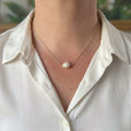 Single white ribbed baroque pearl set at the centre of a delicate sterling silver chain, worn with an open-neck white shirt, showing natural concentric ridges and a soft ivory lustre.