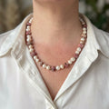 White baroque pearl necklace with irregular pink opal stones showing dark natural mottling and small sterling silver spacers, worn with an open-neck white shirt.