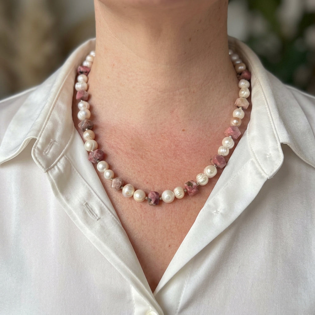 White baroque pearl necklace with irregular pink opal stones showing dark natural mottling and small sterling silver spacers, worn with an open-neck white shirt.