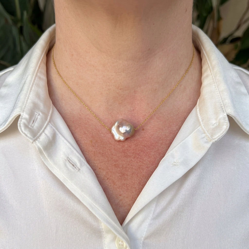 Silvery-blush keshi pearl on a delicate gold-plated sterling silver chain, worn with an open-neck white shirt, showing its irregular ruffled outline and bright iridescent lustre.⠋