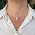 Silvery-blush keshi pearl on a delicate gold-plated sterling silver chain, worn with an open-neck white shirt, showing its irregular ruffled outline and bright iridescent lustre.⠋