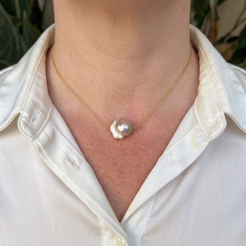 Silvery-blush keshi pearl on a delicate gold-plated sterling silver chain, worn with an open-neck white shirt, showing its irregular ruffled outline and bright iridescent lustre.⠋